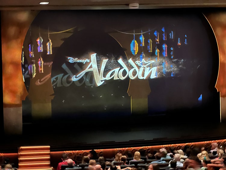 a view of the Walt Disney Theatre stage reading "Aladdin" before the start of the performance on Disney Wish
