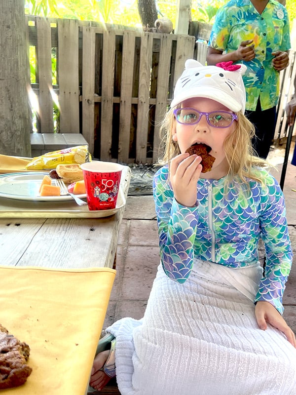 a girl with wet hair wearing a rash guard and towel eating a large cookie at a picnic table