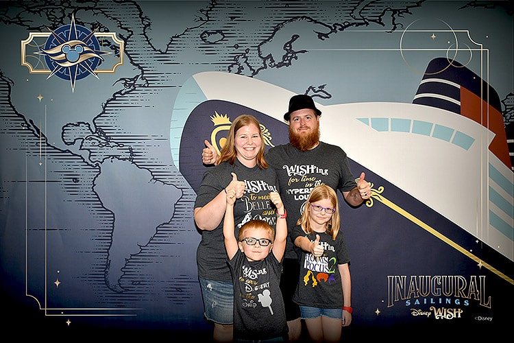 a family of four in matching t-shirts posing in front of a cruise ship backdrop