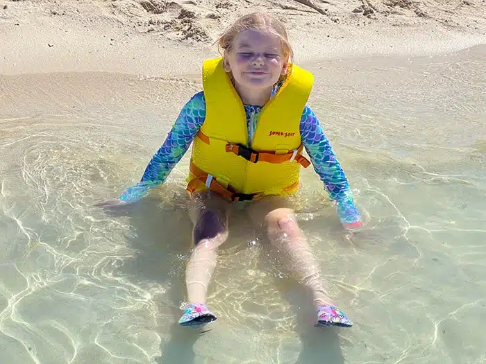 young girl in a yellow life vest sitting in the ocean near the shore