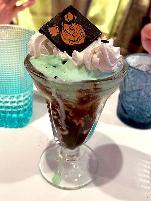 a dessert called It's Elsa's Coronation Sundae from the Arendelle restaurant on the Disney Wish with a chocolate square featuring a pumpkin Mickey head on top