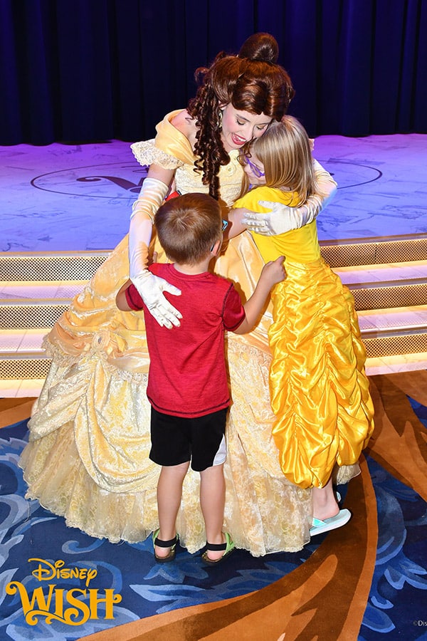 two children, including a girl in a golden gown, hugging Belle from Beauty and the Beast