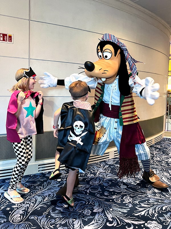 a boy and girl dressed as pirates running into Goofy dressed as a pirate on the Disney Wish ship