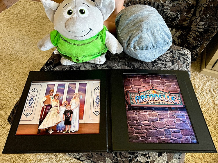 a rock troll plush in both troll form and rock form sitting above a leather photo book featuring Frozen characters and the Arendelle restaurant sign
