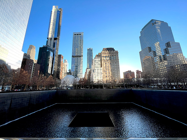 one of the 9/11 memorial pools at the site of where the twin towers fell in NYC with tall buildings in the background