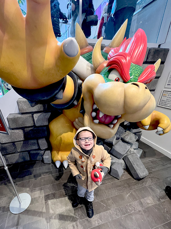 a boy standing in front of a large Bowser statue at the Nintendo Store in NYC