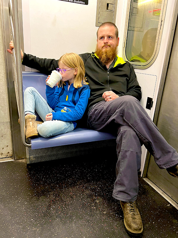 a father sitting next to his daughter who is sipping on hot cocoa while riding the subway in New York City