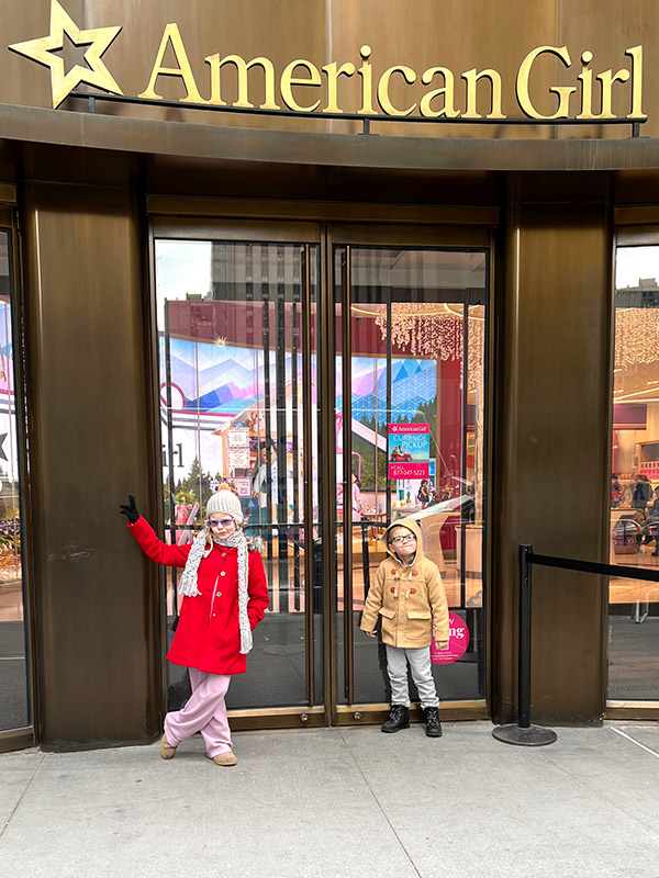 a boy and girl standing outside the entrance to American Girl Place in New York City