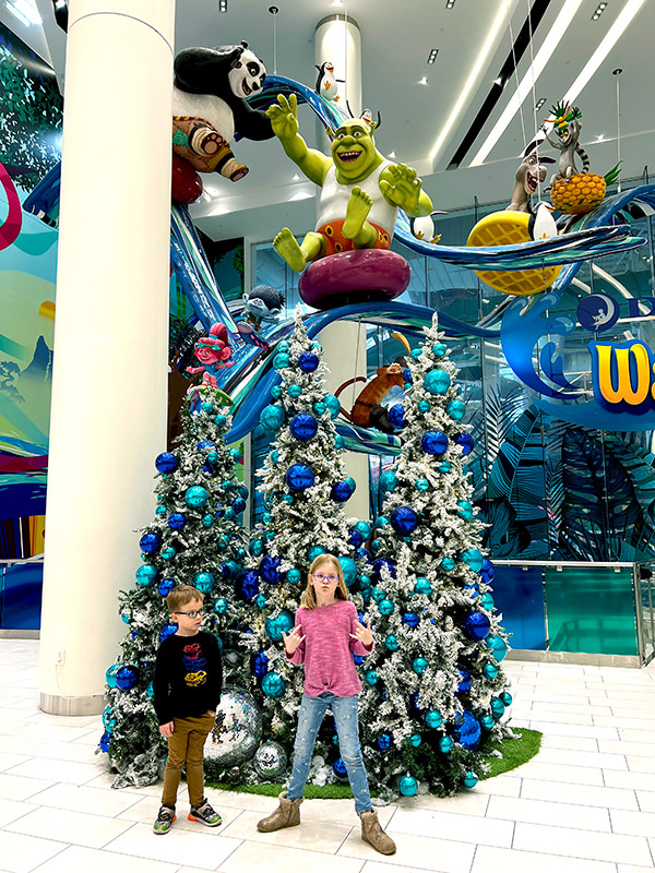a boy and girl posing in front of a blue-themed Christmas tree in front of the DreamWorks Water Park at the American Dream Mall