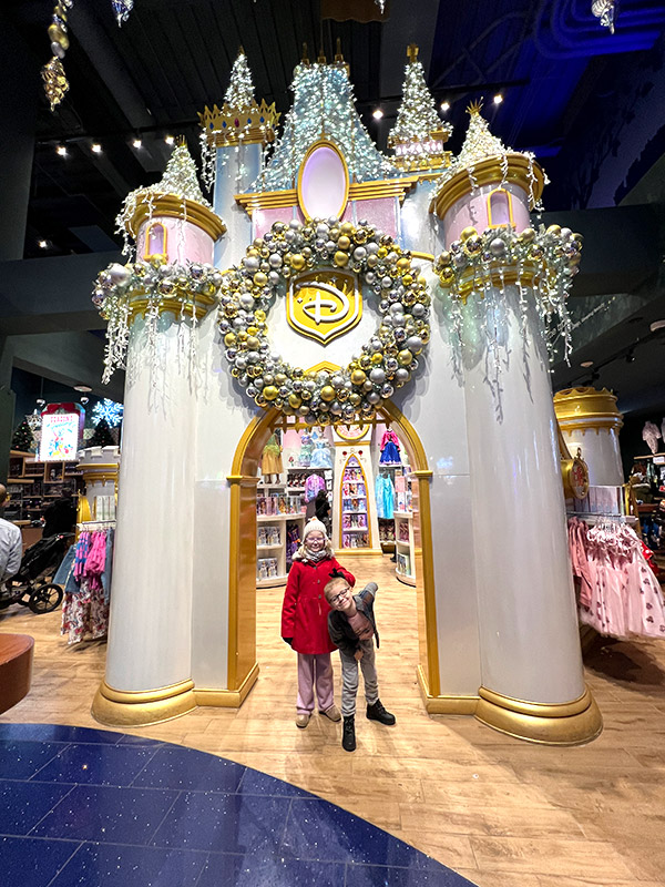 a girl and boy posing under the archway of the fairytale castle facade decorated for Christmas at the Disney Store in Times Square