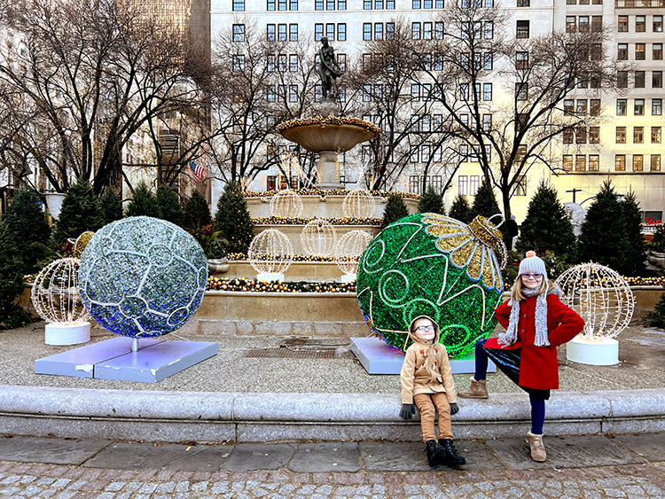 kids posing in front of giant ornaments made of Christmas lights at the Pulitzer Plaza in New York City