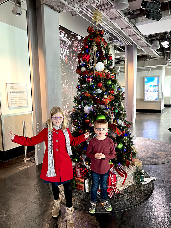kids posing with a Christmas tree inside the Empire State Building in NYC