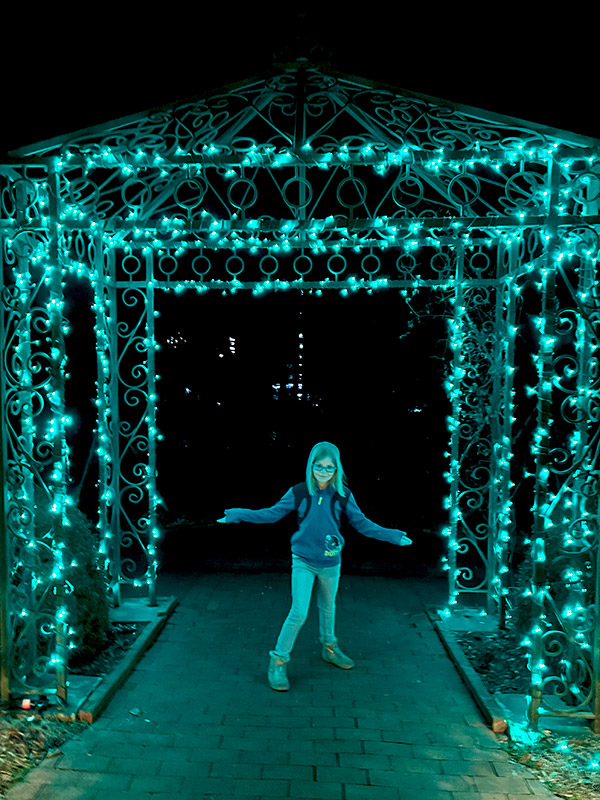 a girl posing under an archway covered in blue Christmas lights at New York Botanical Gardens GLOW