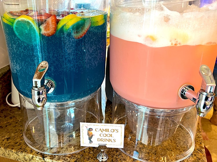 two large drink dispensers containing blue and pink punches with card featuring Camilo from Encanto and the text "Camilo's cool drinks"