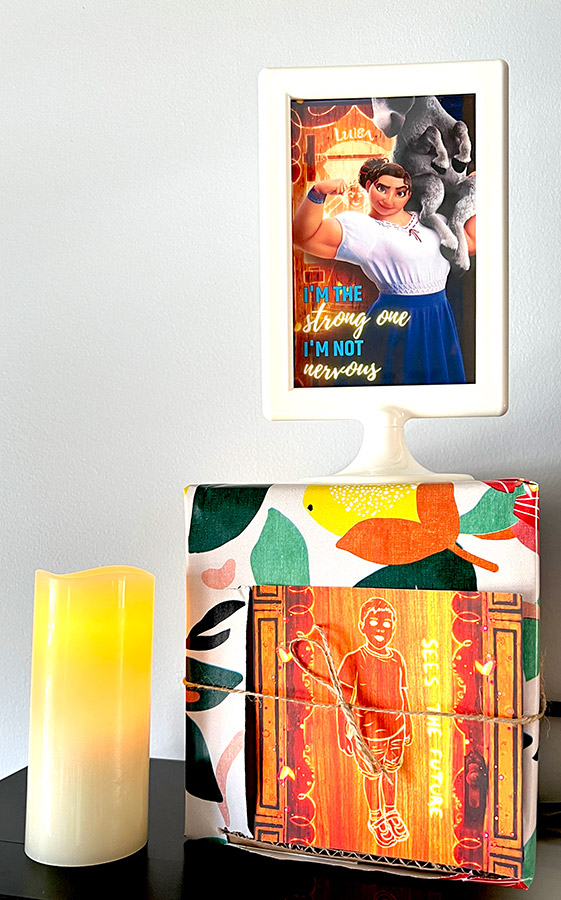 a glowing LED candle next to a gift box with a custom glowing Encanto door with a framed photo of Luisa sitting on top