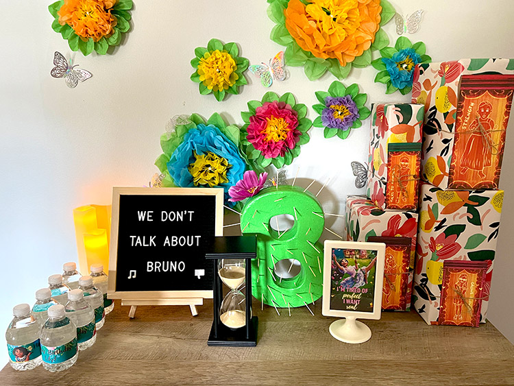 a cabinet full of Encanto birthday party decor including an hourglass, letter board, and paper flowers
