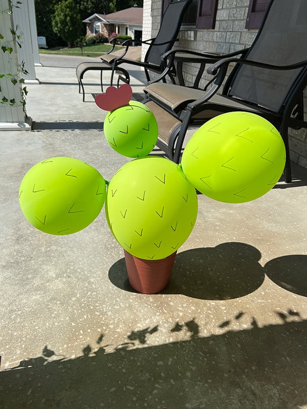 a cactus made out of green balloons inside a planter with a pink cardstock flower on top