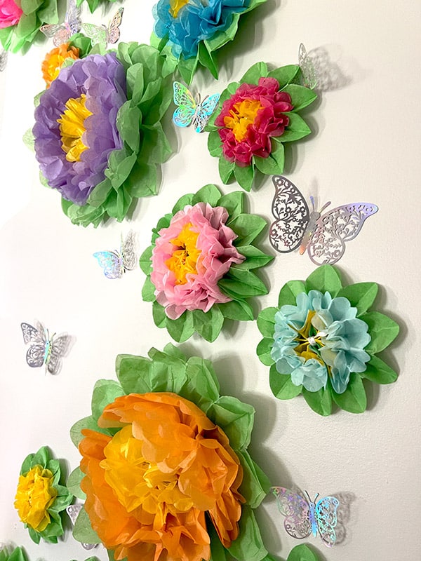 closeup of part of a wall covered in colorful paper flowers and silver butterflies