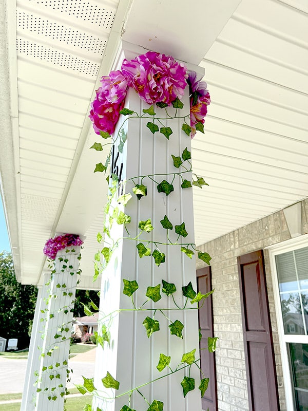 a white porch column wrapped in fake vines with a crown of pink flowers at the top