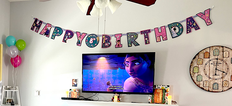 a giant Encanto happy birthday banner hanging over a living room TV on the wall
