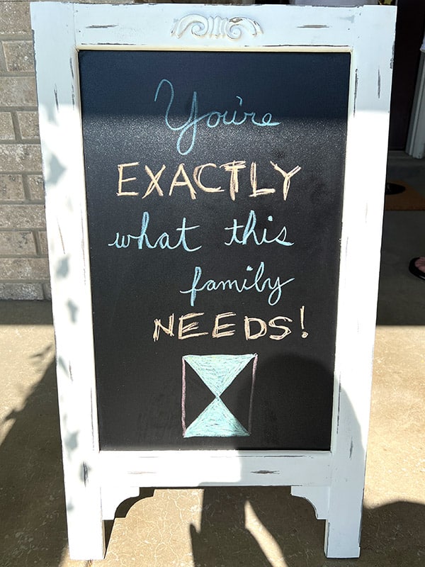 standing chalkboard sign that says "You're exactly what this family needs!" with an hourglass drawn in chalk