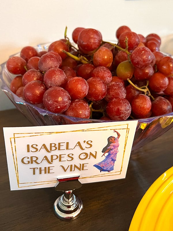 a bowl full of grapes still on vines and a card featuring Isabela from Encanto and the text "Isabela's grapes on the vine"