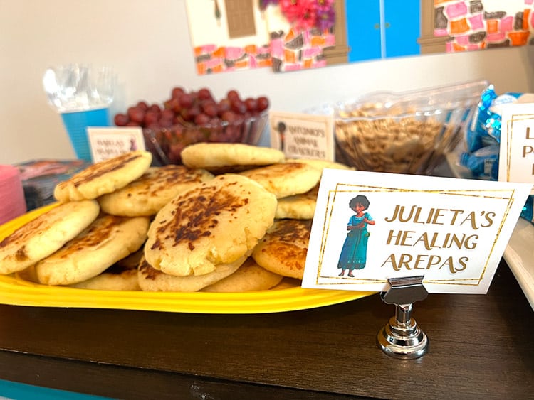 a large tray full of arepas con queso and a card featuring Julieta from Encanto and the text "Julieta's healing arepas"