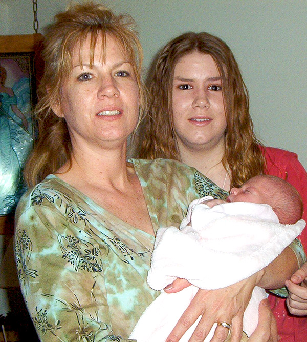 a woman holding a newborn baby with a younger woman standing behind her