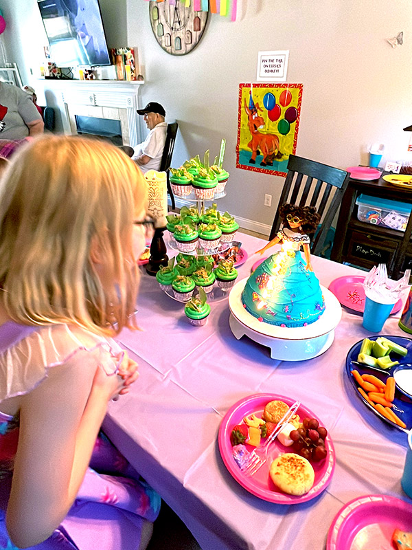 a little girl about to blow out her birthday candles on an Encanto cake made to look like Mirabel