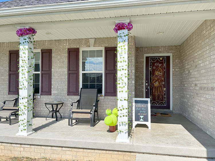 a front porch with columns wrapped in vines and flowers, a potted cactus made from balloons, and a chalkboard welcome sign