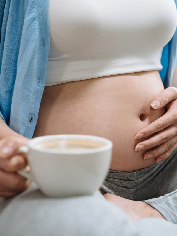 closeup of a pregnant woman's belly in the second trimester as she holds a cup of chai tea on her knee