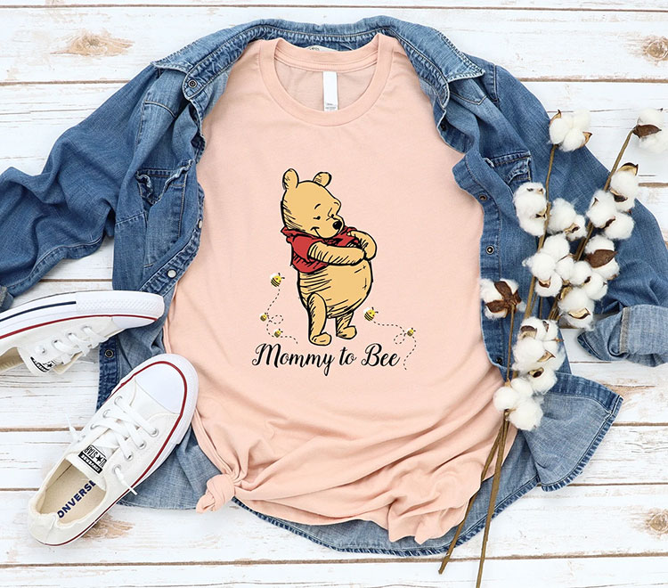 peach-colored shirt featuring Winnie the Pooh holding his stomach with the text "Mommy to Bee"