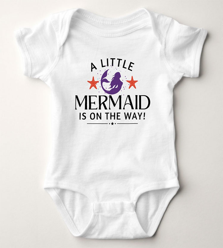 a white baby bodysuit featuring a purple mermaid and pink stars and black text reading "A little mermaid is on the way!"