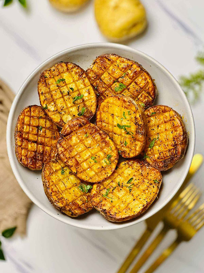 roasted potato haves with criss cross lines cut across them, piled in a white bowl