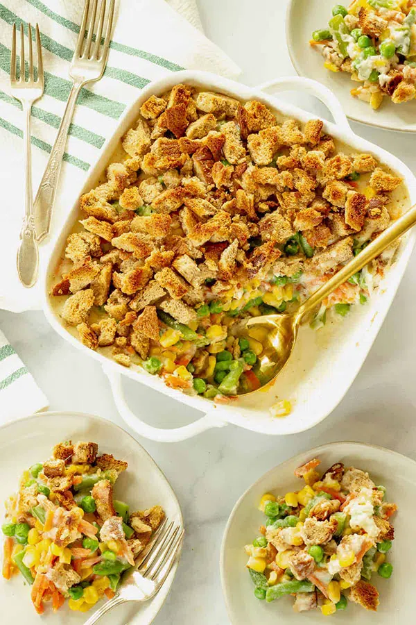 a casserole of mixed vegetables covered in bread crumbs with a couple of smaller plates of the food next to it