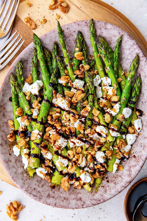 a bowl full of roasted asparagus that's been covered in goat cheese, chopped walnuts, and a drizzle of Balsamic