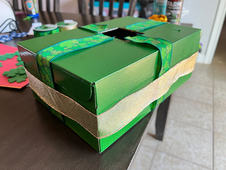 a green shoebox wrapped in green and gold craft ribbon
