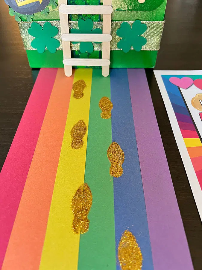 gold glitter leprechaun tracks on a rainbow road leading to a leprechaun trap