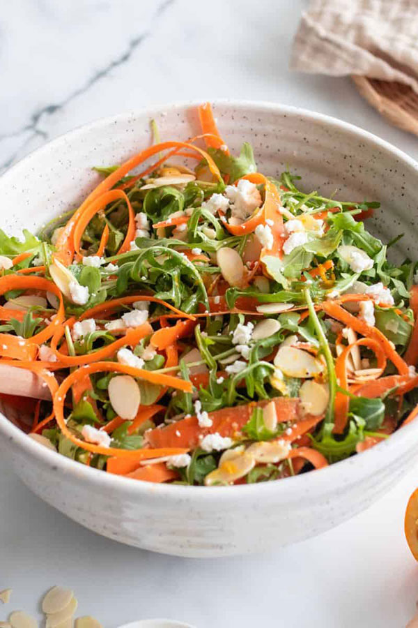 a white bowl full of salad with ribboned carrots and arugula