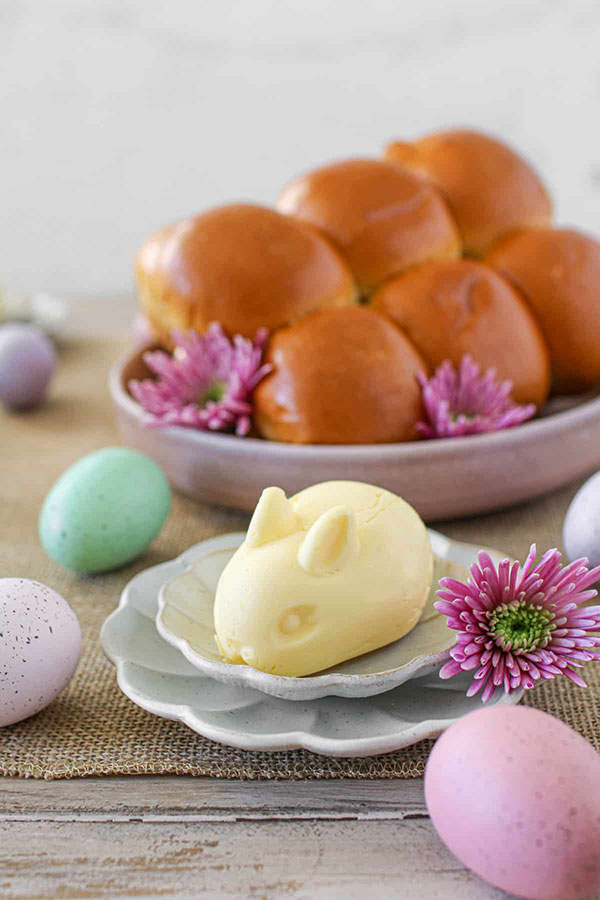 a mound of butter molded to look like a baby bunny, with a bowl of rolls behind it