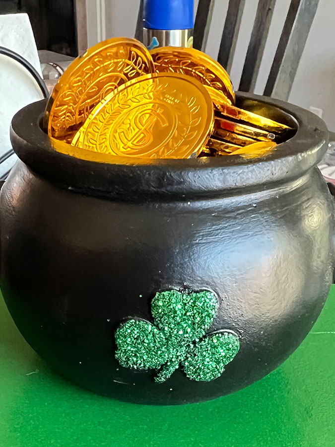 a black pot of gold with a green shamrock on the front, full of plastic gold coins