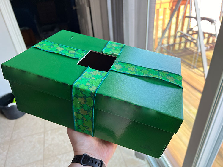 a green shoebox with shamrock-printed craft ribbon wrapped around it