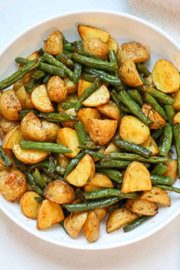 a large white bowl full of roasted potato chunks and green beans