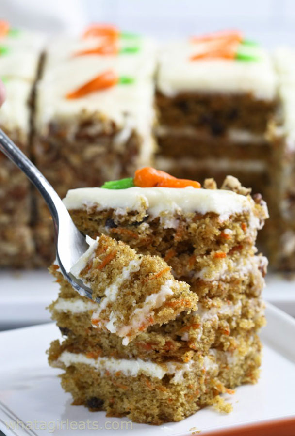 a slice of four-layer carrot cake with a small frosting carrot on top