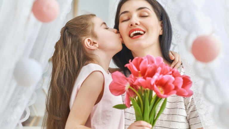 a little girl kissing her mother while holding a bouquet of pink flowers