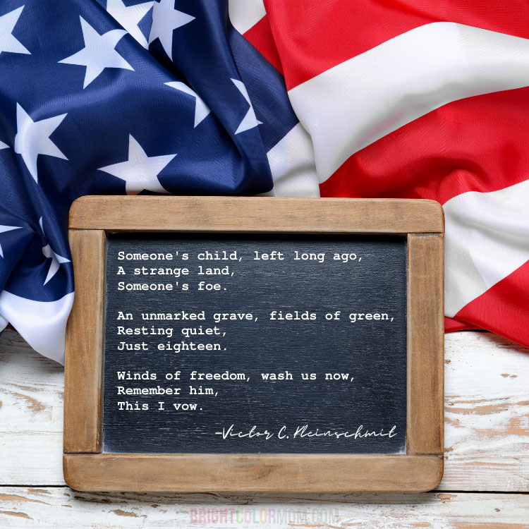a flat lay on white wood of an American flag and a small wooden-framed chalkboard with a poem: "Someone's child, left long ago, A strange land, Someone's foe. An unmarked grave, fields of green, Resting quiet, Just eighteen. Winds of freedom, wash us now, Remember him, This I vow. –Victor C. Kleinschmit"