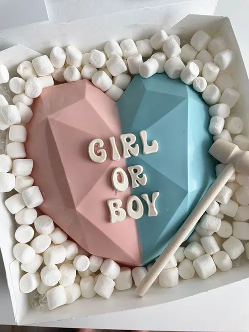 a pink and blue chocolate heart says "girl or boy" surrouneded by marshmallows with a small white hammer