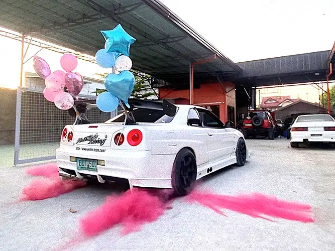 a white car doing a burnout to reveal pink smoke and powder at a gender reveal