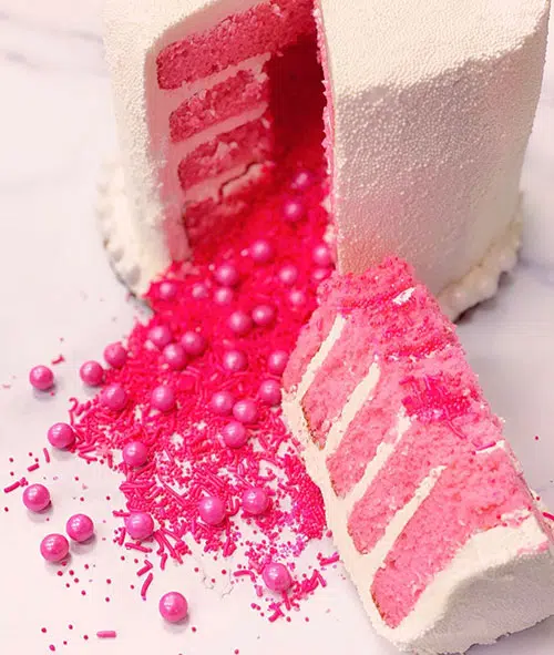 a white cake with a slice cut out to reveal pink candies pouring out