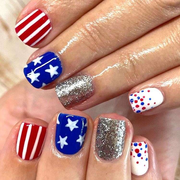 square nails with gel polish, each nail different including red and white stripes, blue with white stars, silver glitter, and white with red and blue dots